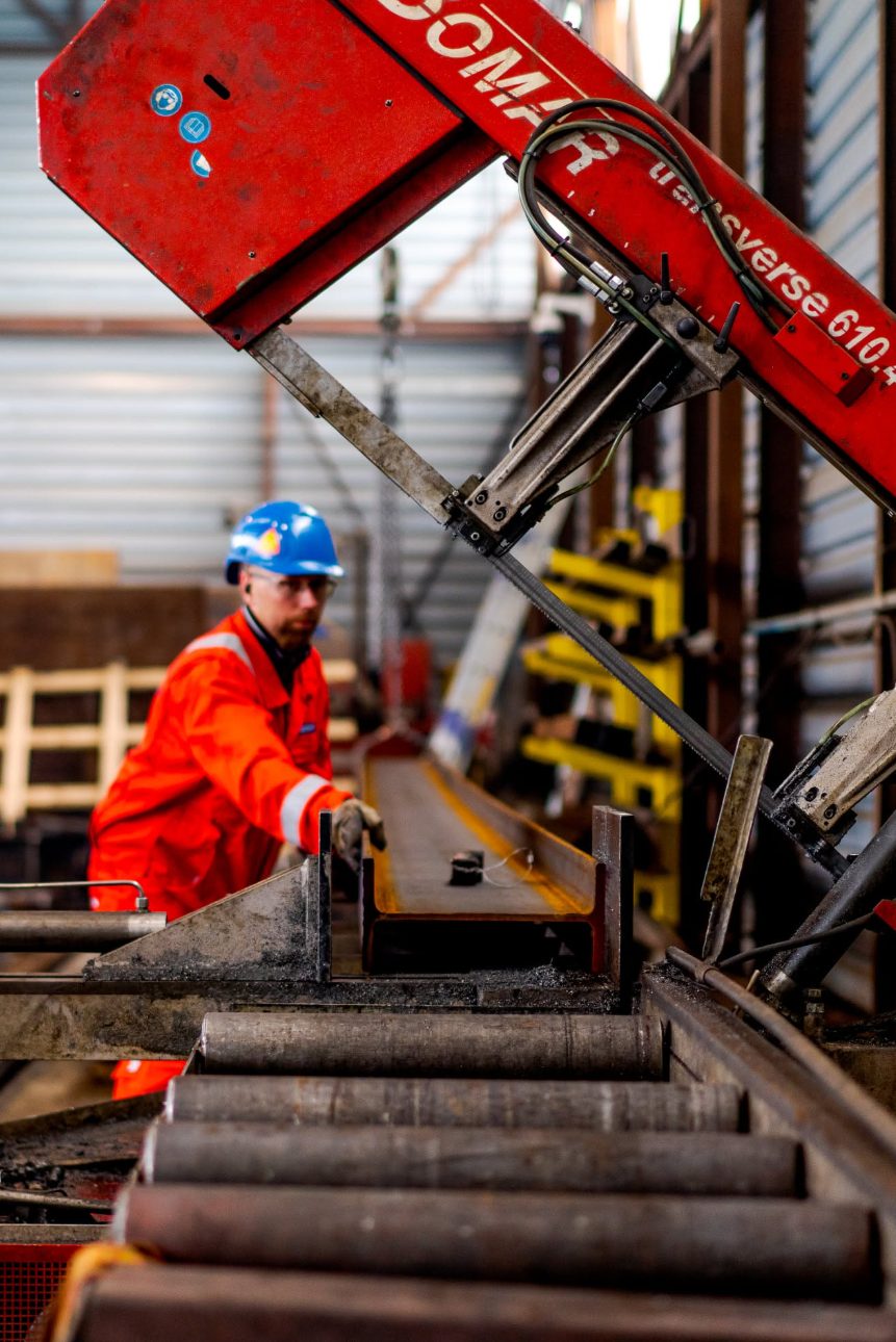 Worker cutting a steel beam on a band saw